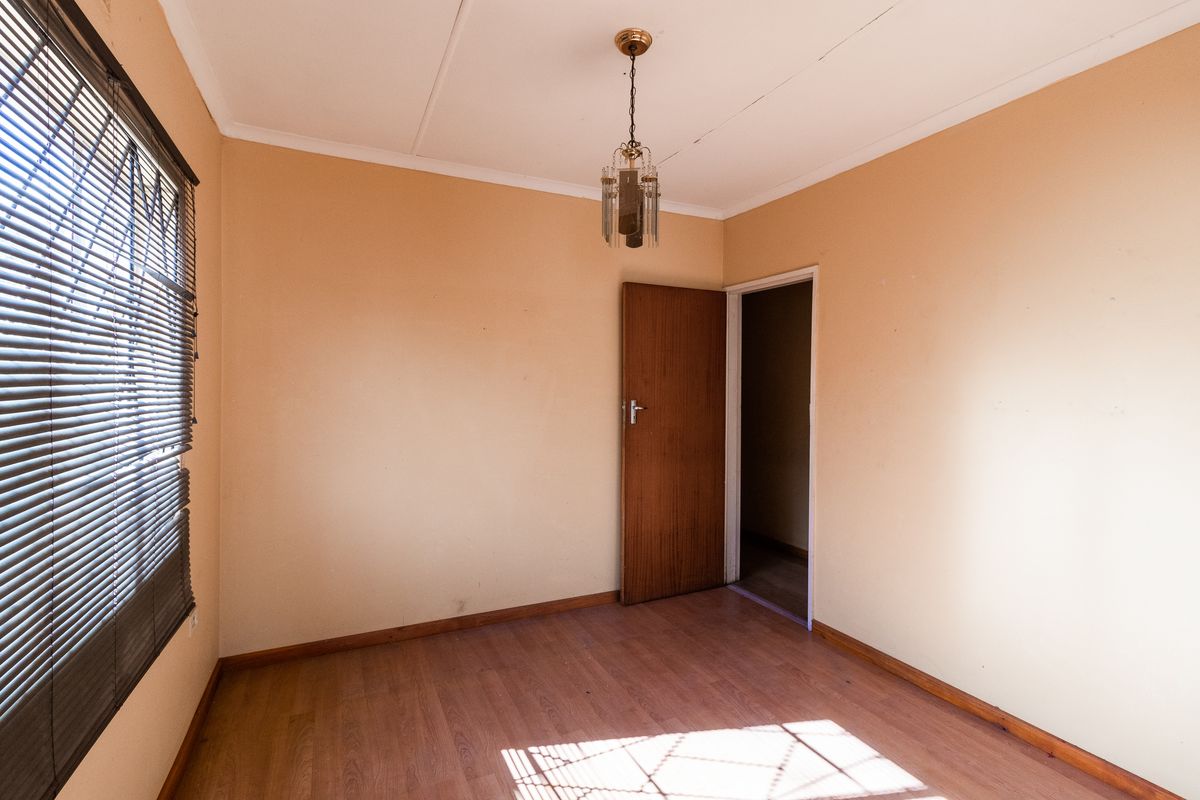 A vacant bedroom featuring laminate flooring, a single pendant light fixture, and a window fitted with horizontal blinds.
