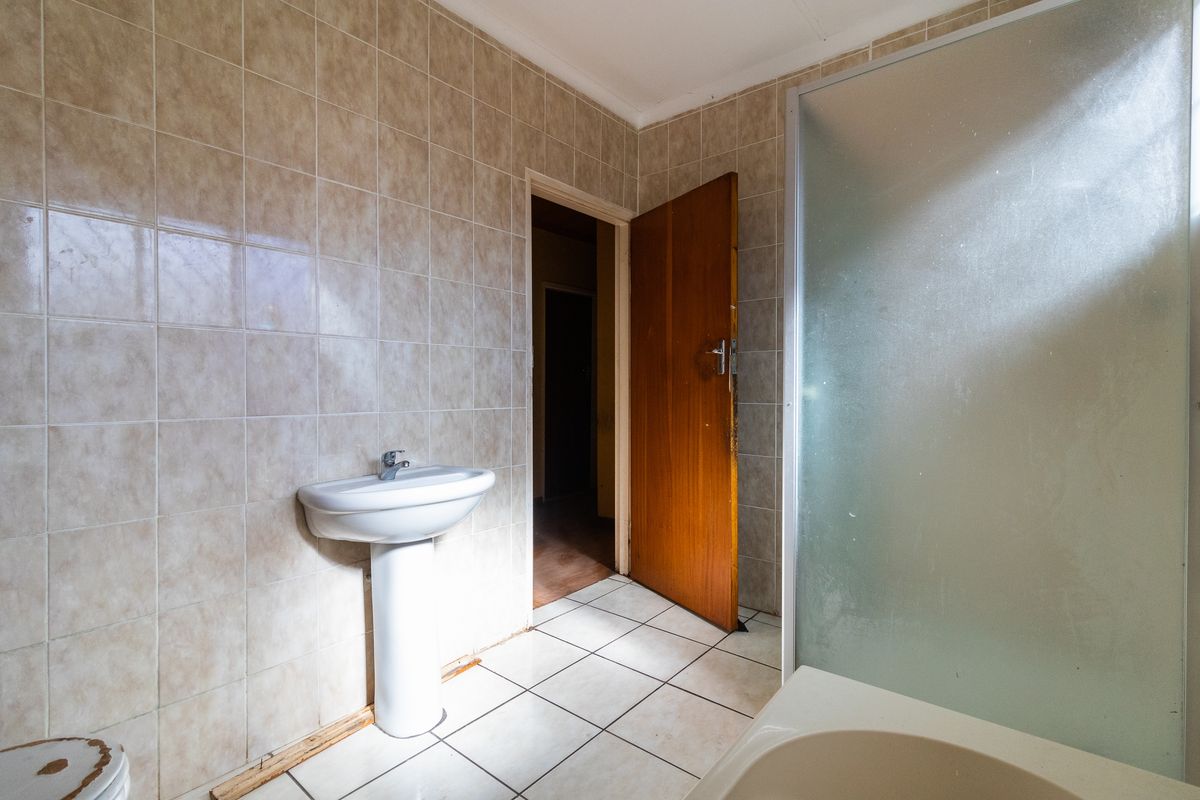 A dated bathroom featuring a pedestal sink, shower enclosure, and tiled walls, requiring cosmetic updates to modernize the space.
