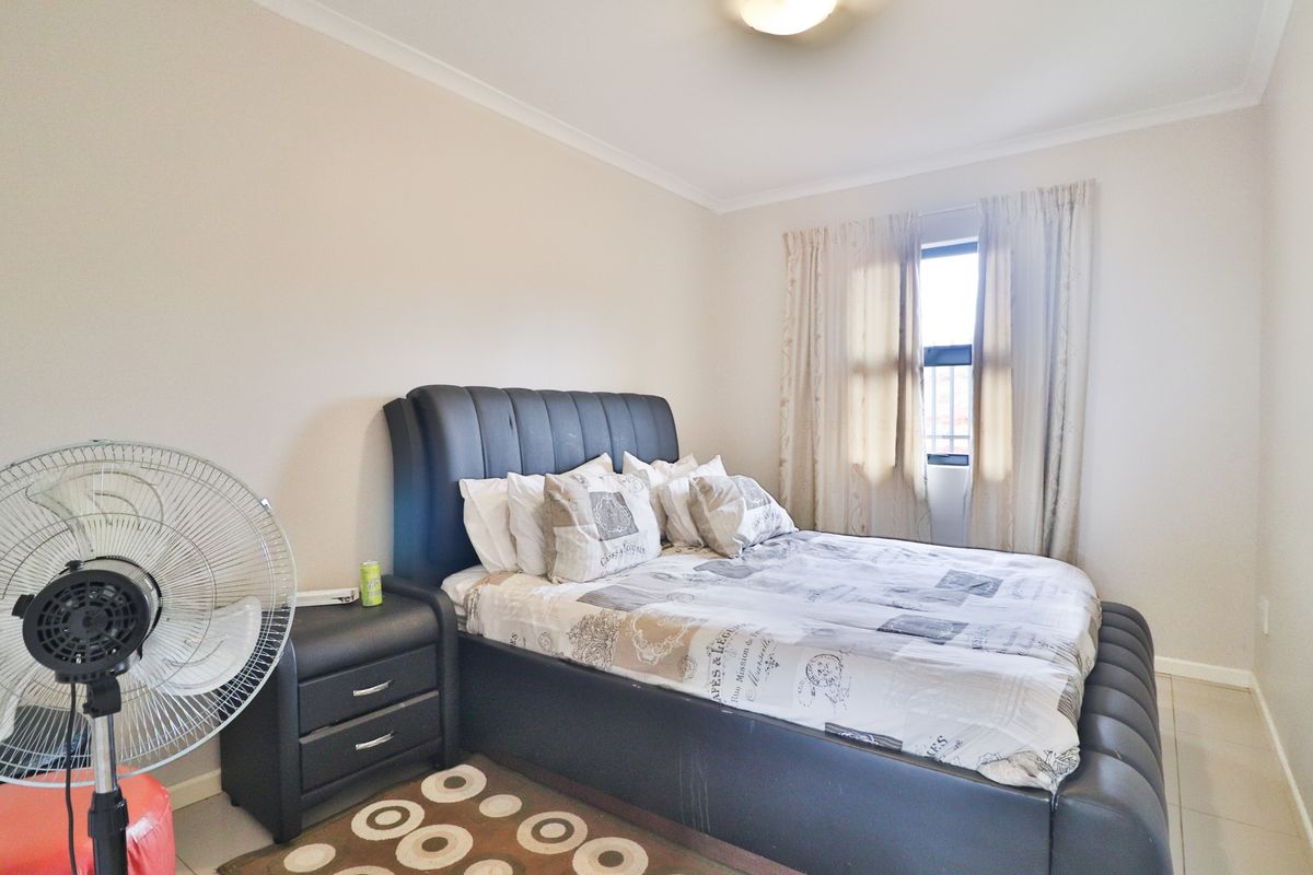 A well-lit bedroom featuring neutral wall tones, tiled flooring, and a window with curtain treatments.