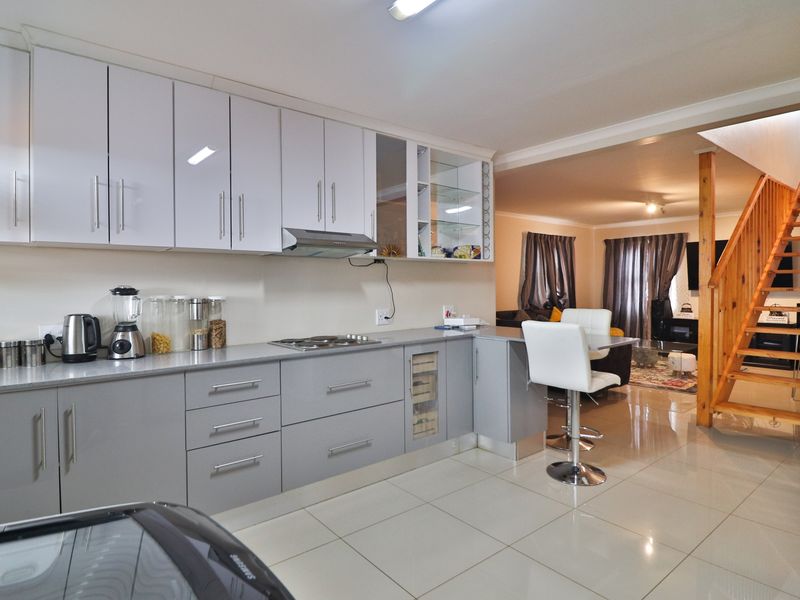 Modern open-plan kitchen featuring sleek grey cabinetry, integrated hob, extractor fan, and polished floor tiles, seamlessly flowing into the adjacent living area with staircase.