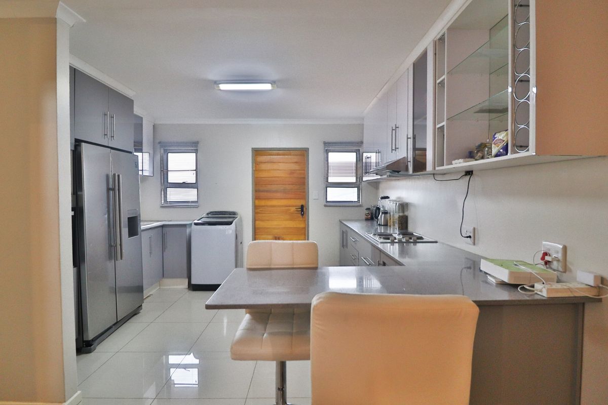 Modern kitchen featuring sleek grey cabinetry, stone countertops, a built-in hob, and tiled flooring, with an integrated breakfast bar and laundry area.