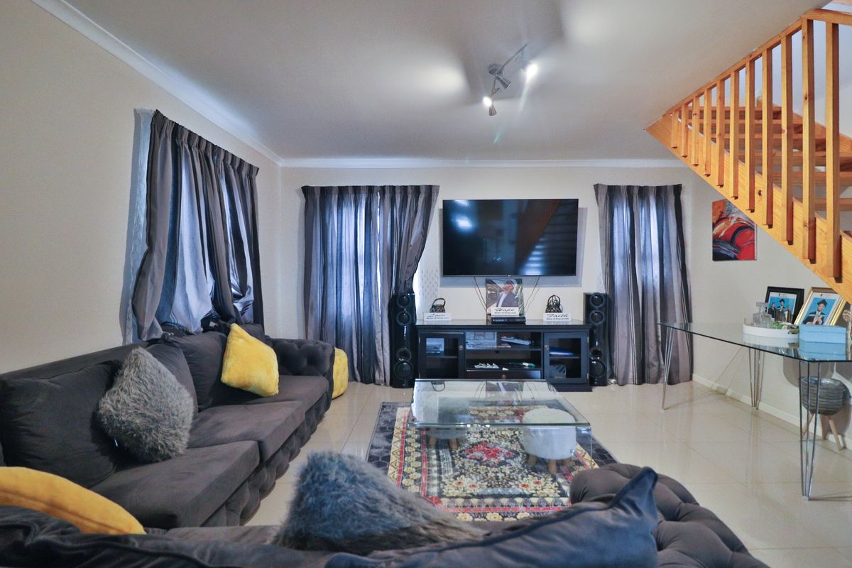 Spacious living room featuring tiled flooring, neutral walls, and a wooden staircase leading to the upper level.