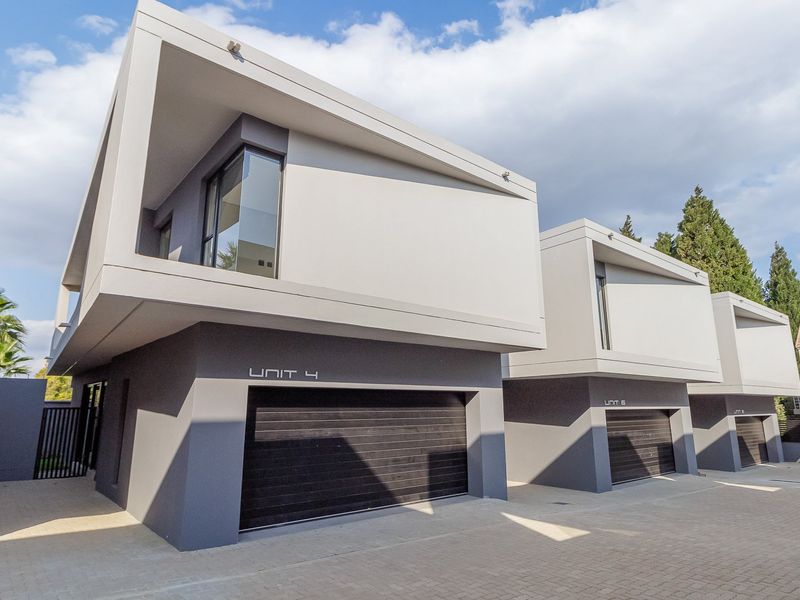 Modern townhouse complex featuring contemporary architectural design, clean lines, paved driveway access, and secure automated garage doors for each unit.