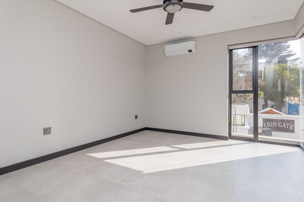 A bright, modern, and empty bedroom featuring neutral tiled flooring, a ceiling fan, a split-system air conditioner, and large sliding glass doors.