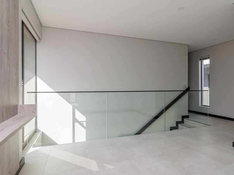 Modern landing area featuring a sleek glass balustrade, tiled flooring, and contemporary timber-look wall accents with recessed lighting.