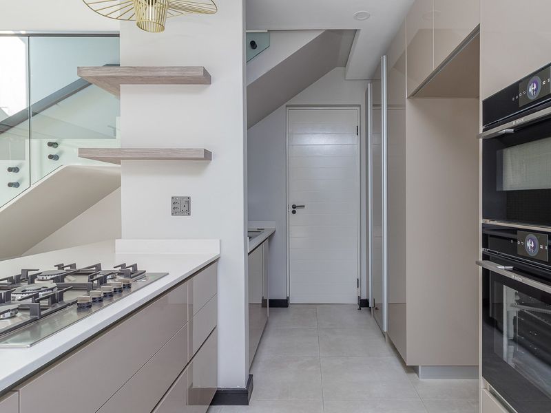 Modern kitchen featuring high-gloss cabinetry, integrated Bosch appliances, gas hob, stone countertops, and a sleek glass balustrade staircase.