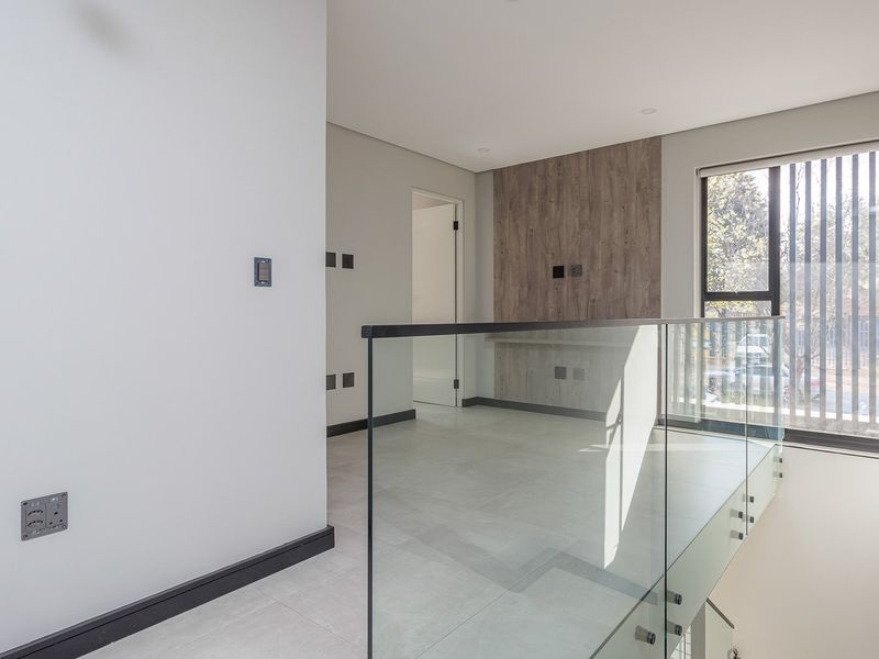 A bright, modern landing area featuring a sleek glass balustrade, neutral tiled flooring, and a contemporary wood-look feature wall panel.