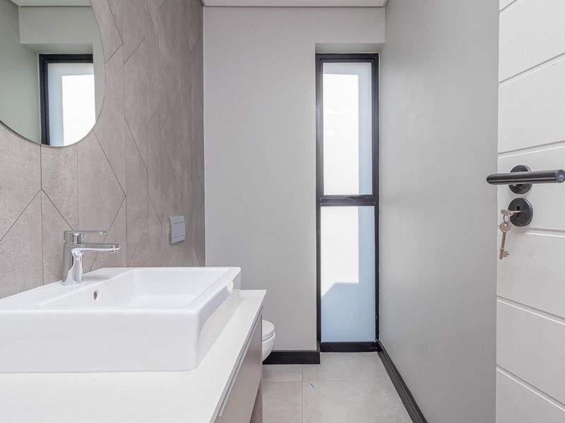 A modern, minimalist guest bathroom featuring a sleek vanity basin, contemporary grey tiled feature wall, and clean, neutral finishes throughout.