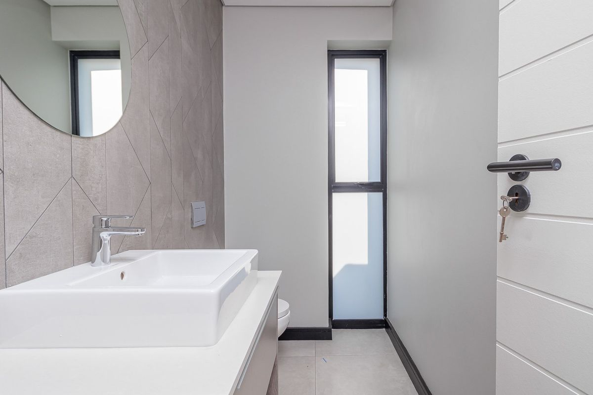 A modern, minimalist guest bathroom featuring a sleek vanity basin, contemporary grey tiled feature wall, and clean, neutral finishes throughout.