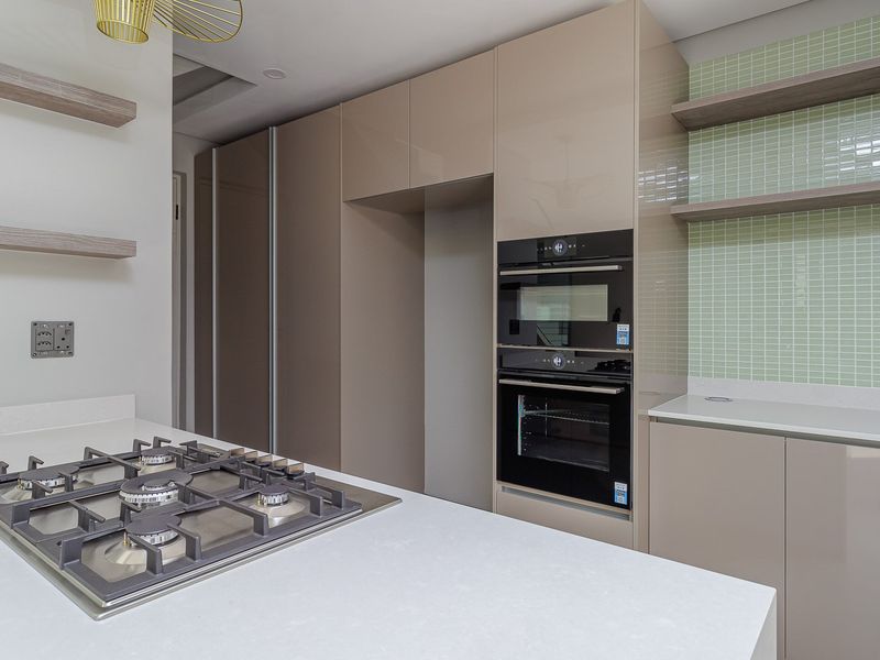 Modern kitchen featuring high-gloss cabinetry, quartz countertops, a built-in gas hob, and integrated oven and microwave units with a stylish mosaic tile backsplash.