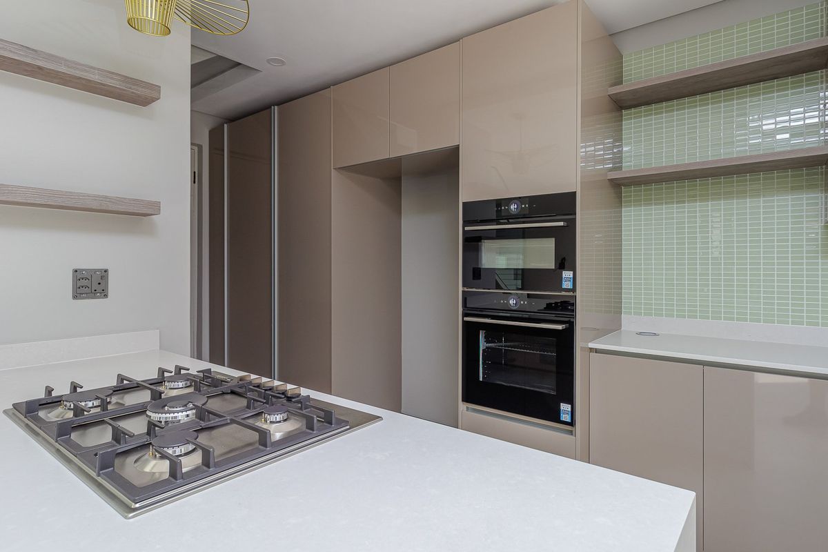 Modern kitchen featuring high-gloss cabinetry, quartz countertops, a built-in gas hob, and integrated oven and microwave units with a stylish mosaic tile backsplash.