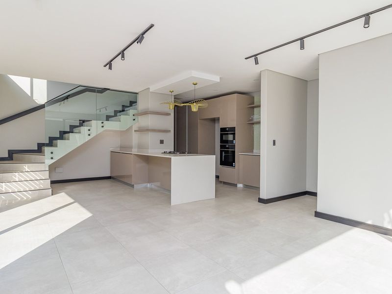 Modern open-plan kitchen and living area featuring sleek cabinetry, built-in appliances, a central island, and a contemporary staircase with glass balustrades.