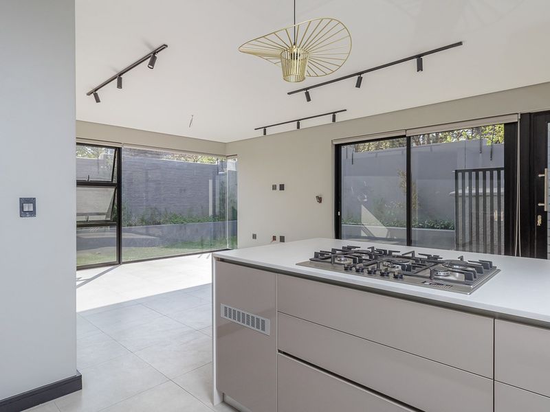 Modern open-plan kitchen and living area featuring a central island with gas hob, sleek cabinetry, track lighting, and large sliding doors to the garden.