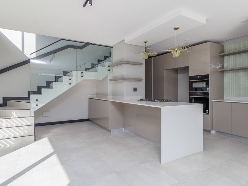 Modern open-plan kitchen featuring sleek cabinetry, integrated appliances, a central island, and a striking staircase with a glass balustrade.
