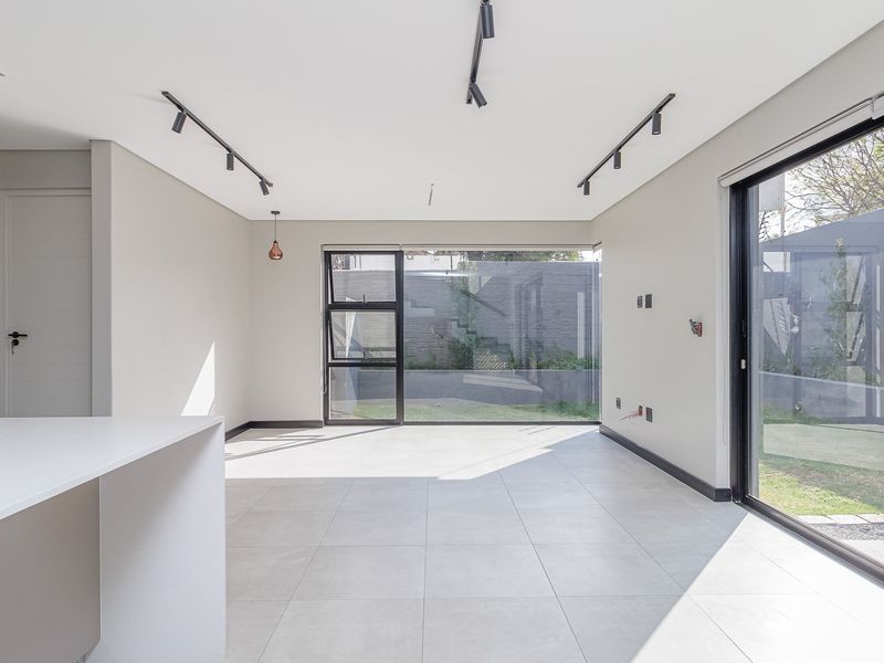 Modern open-plan living area featuring sleek porcelain tiles, track lighting, and large sliding glass doors that provide seamless access to the rear garden.