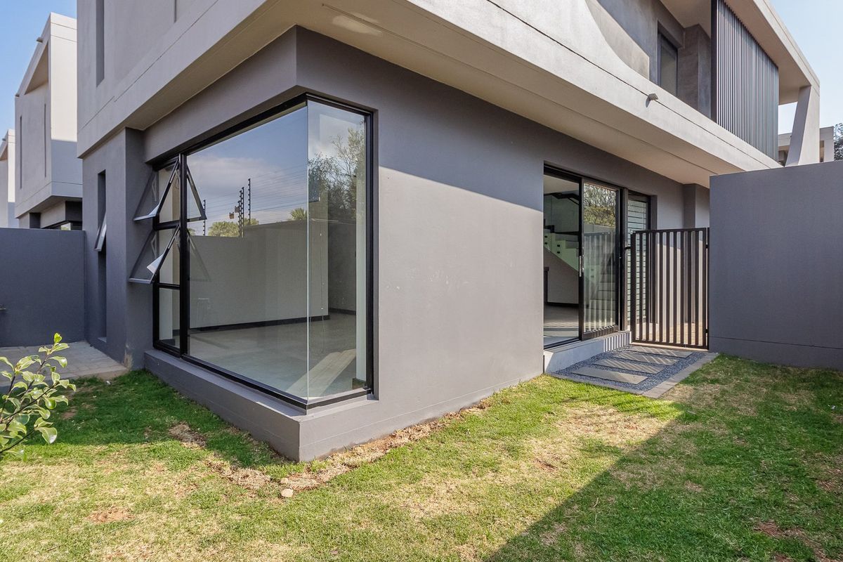 Rear view of a modern townhouse featuring a corner window, sliding glass door access, and a private garden area.
