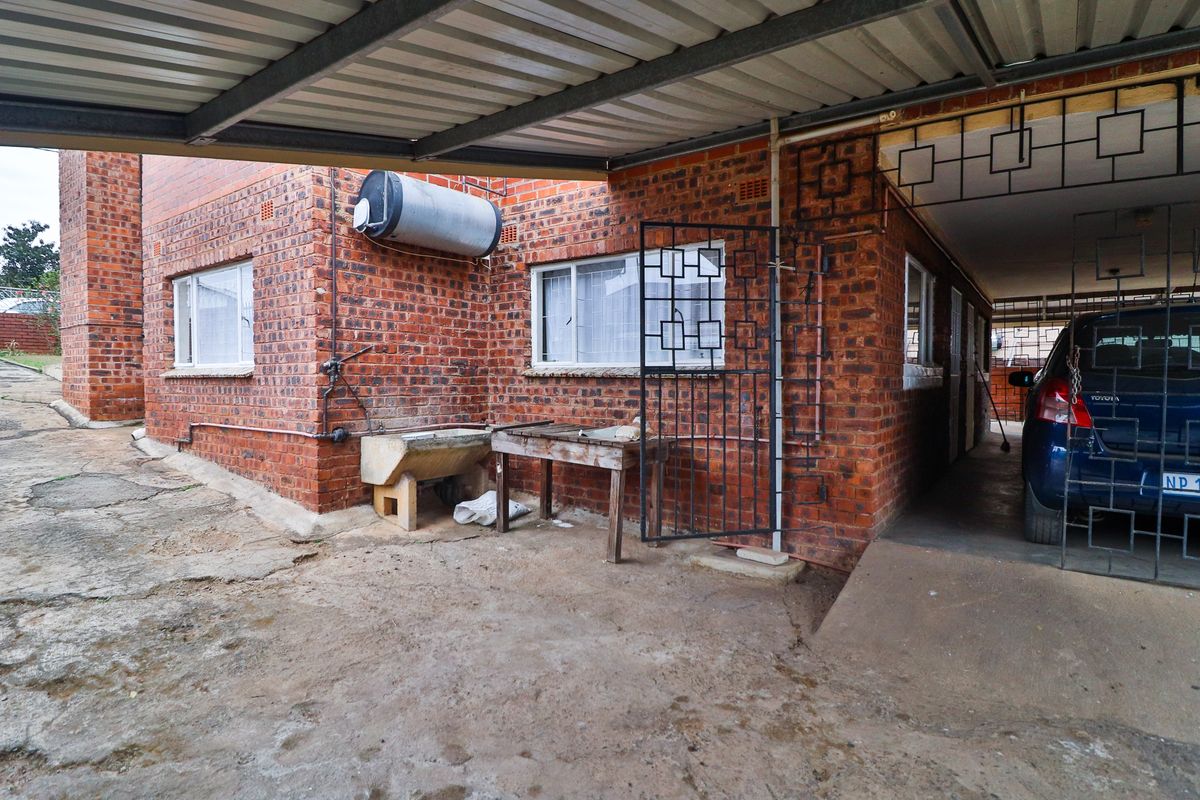 Exterior view of the property featuring a covered carport, exposed brick facade, and external utility area with a concrete wash trough.