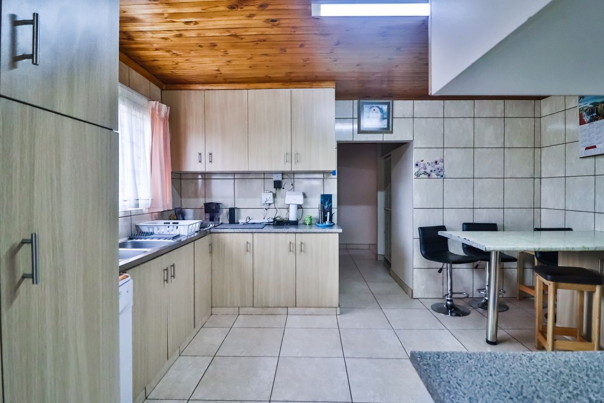 A functional kitchen featuring light-toned cabinetry, tiled flooring, and a wood-paneled ceiling, offering a practical layout with an integrated breakfast bar area.