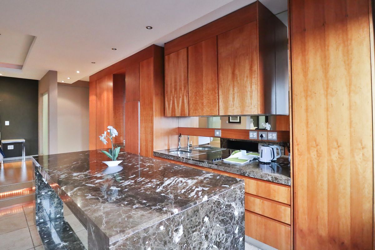 Modern kitchen featuring rich wood cabinetry, a large marble-topped island, integrated storage, and recessed ceiling lighting.