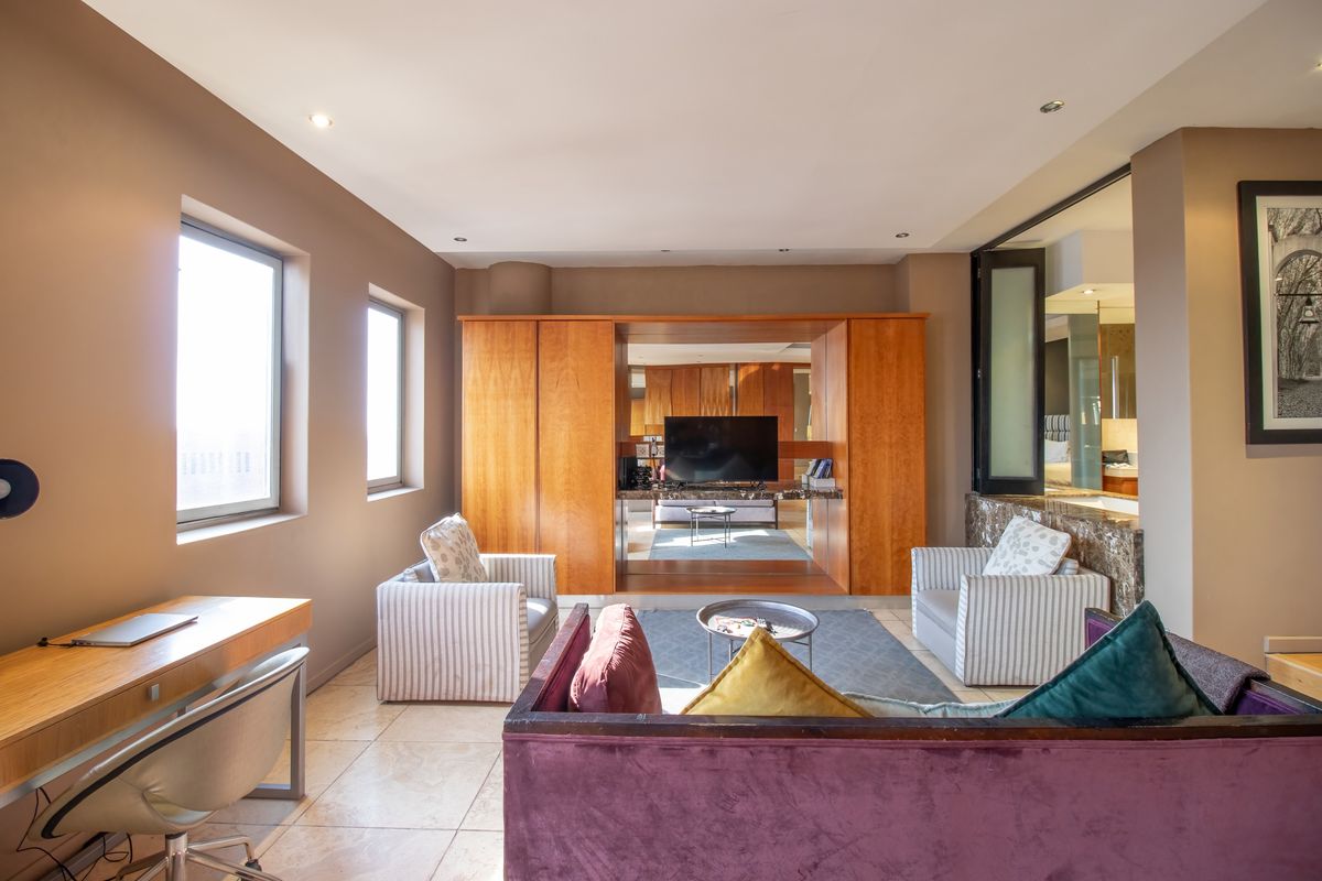 A spacious living area featuring built-in wooden cabinetry, tiled flooring, recessed lighting, and an integrated glass-partitioned bathroom suite.