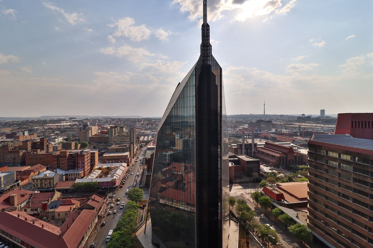 Aerial view of a modern glass skyscraper situated within a dense urban cityscape.