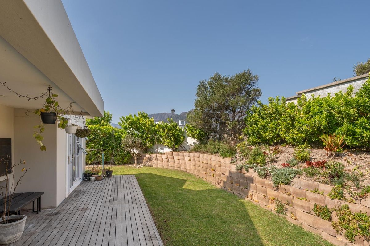 A well-maintained rear garden featuring a timber deck, a built-in outdoor fireplace, and a tiered retaining wall with established landscaping.