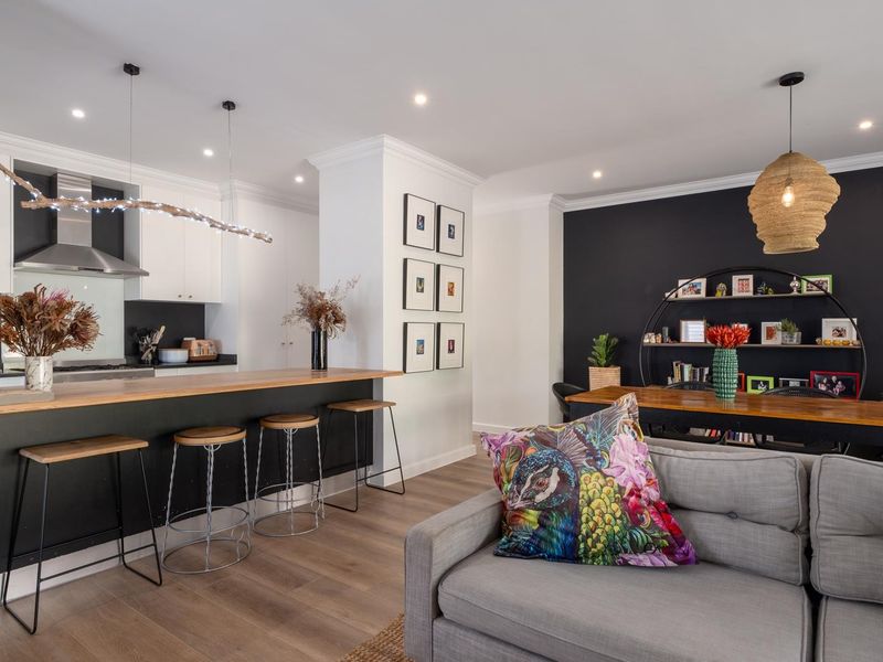 Modern open-plan living area featuring a kitchen with a breakfast bar, timber flooring, and recessed lighting, seamlessly connecting to the dining and lounge space.