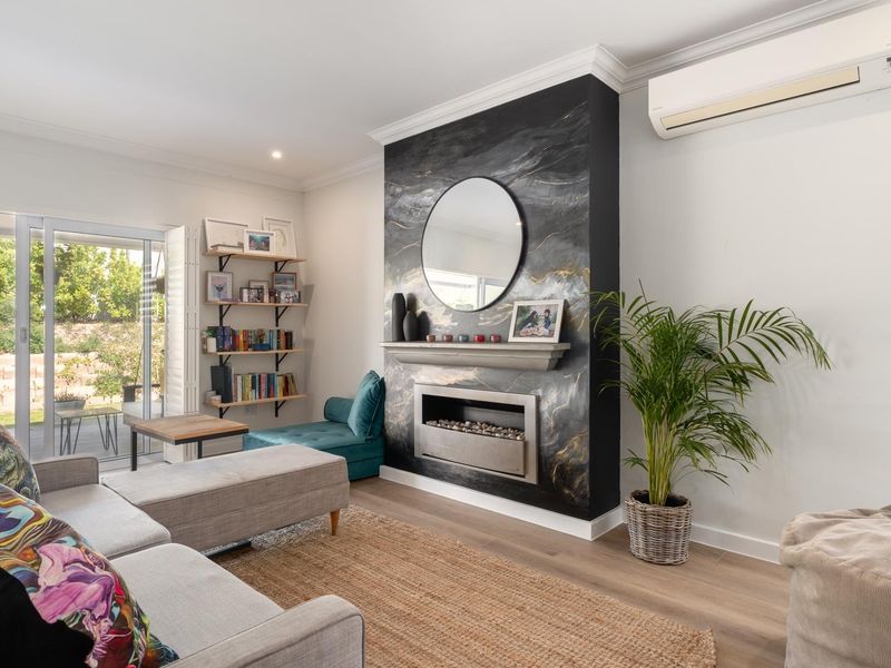 A bright living room featuring a striking marble-look fireplace surround, timber flooring, and sliding glass doors providing direct access to the outdoor patio area.