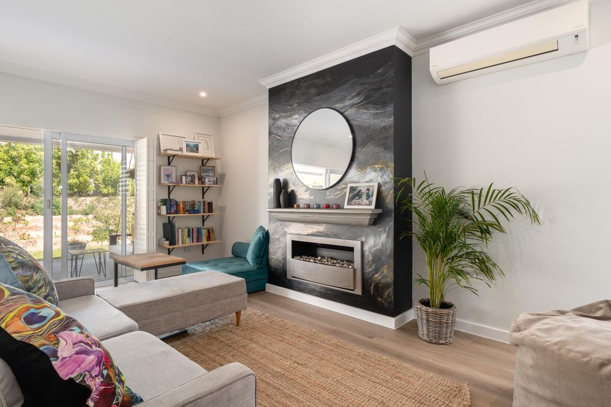 A bright living room featuring a striking marble-look fireplace surround, timber flooring, and sliding glass doors providing direct access to the outdoor patio area.