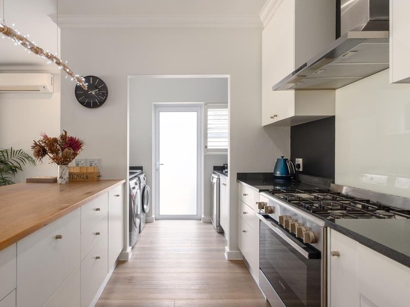 Modern kitchen featuring stone countertops, a timber breakfast bar, gas hob, and integrated extractor fan, with an adjoining scullery area.