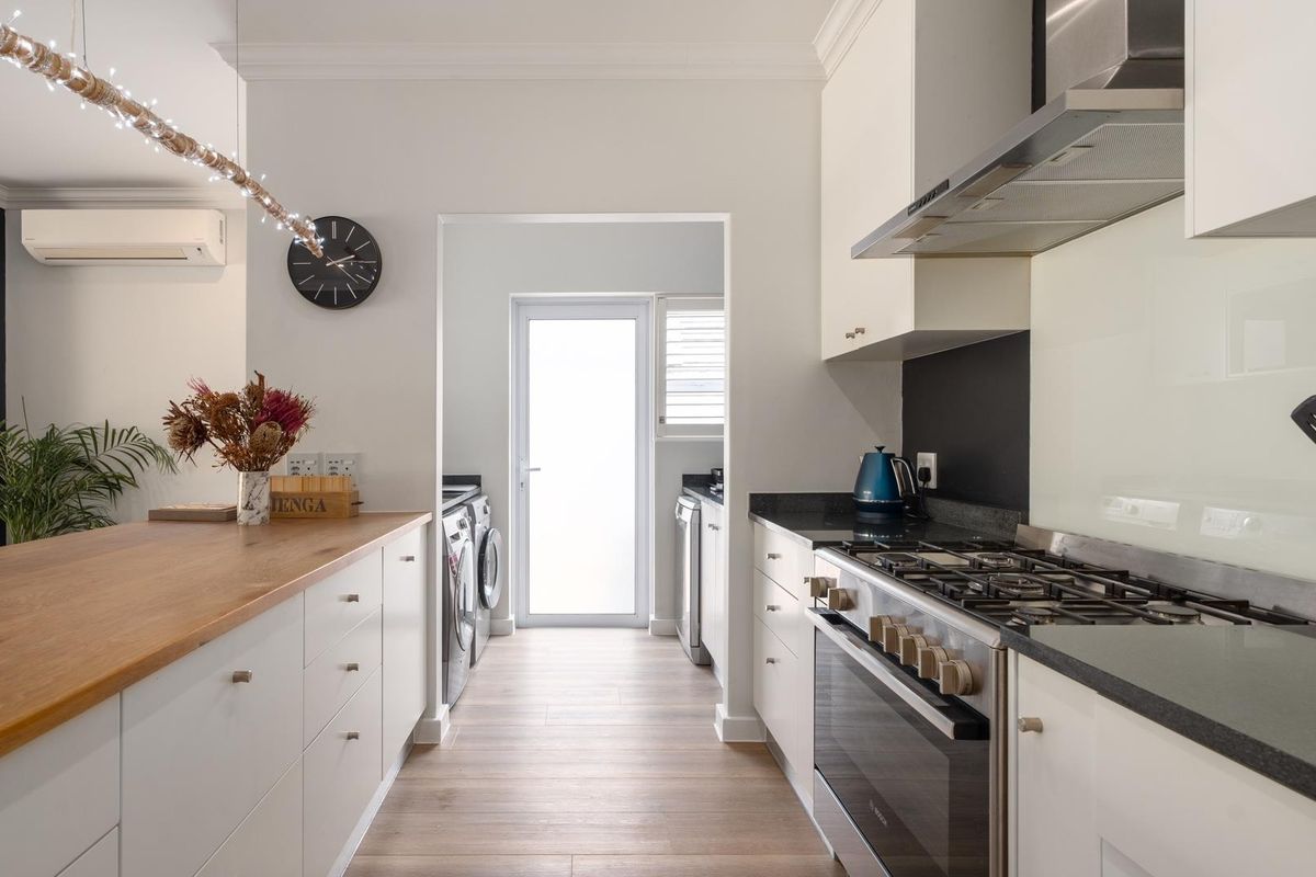 Modern kitchen featuring stone countertops, a timber breakfast bar, gas hob, and integrated extractor fan, with an adjoining scullery area.
