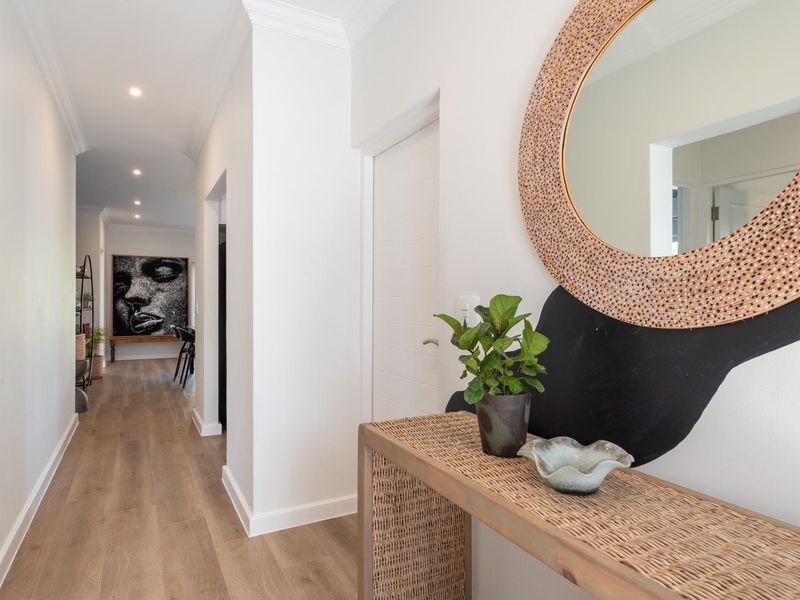 A bright and modern hallway featuring light-toned laminate flooring, crisp white walls, and recessed downlighting, leading through to the main living areas.
