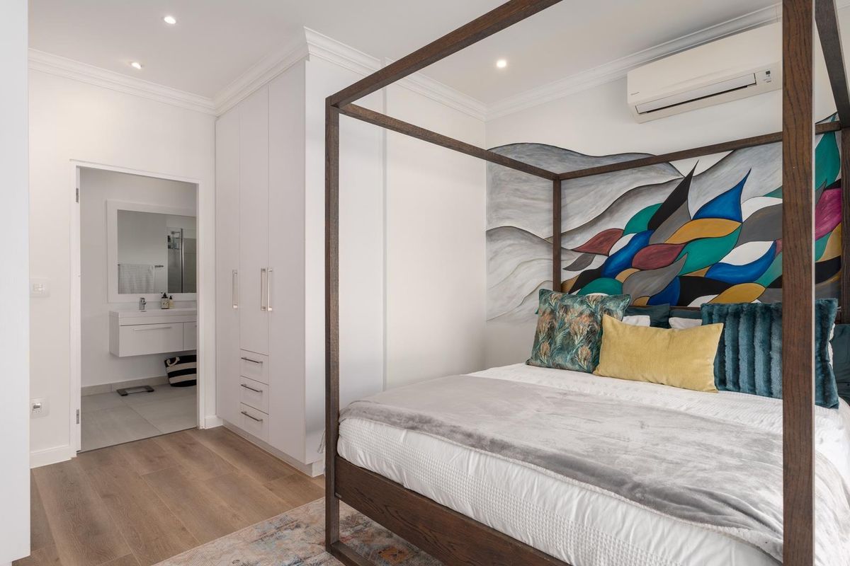 A well-maintained bedroom featuring laminate flooring, built-in cupboards, recessed lighting, and a split-system air conditioner, with direct access to an en-suite bathroom.