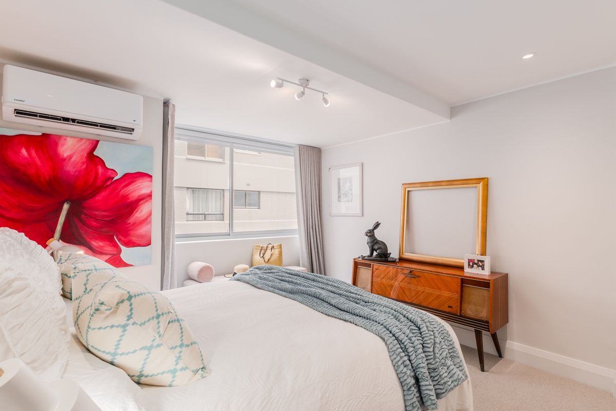 A bright and well-maintained bedroom featuring a wall-mounted air conditioning unit, recessed ceiling lighting, and large windows allowing for natural light.