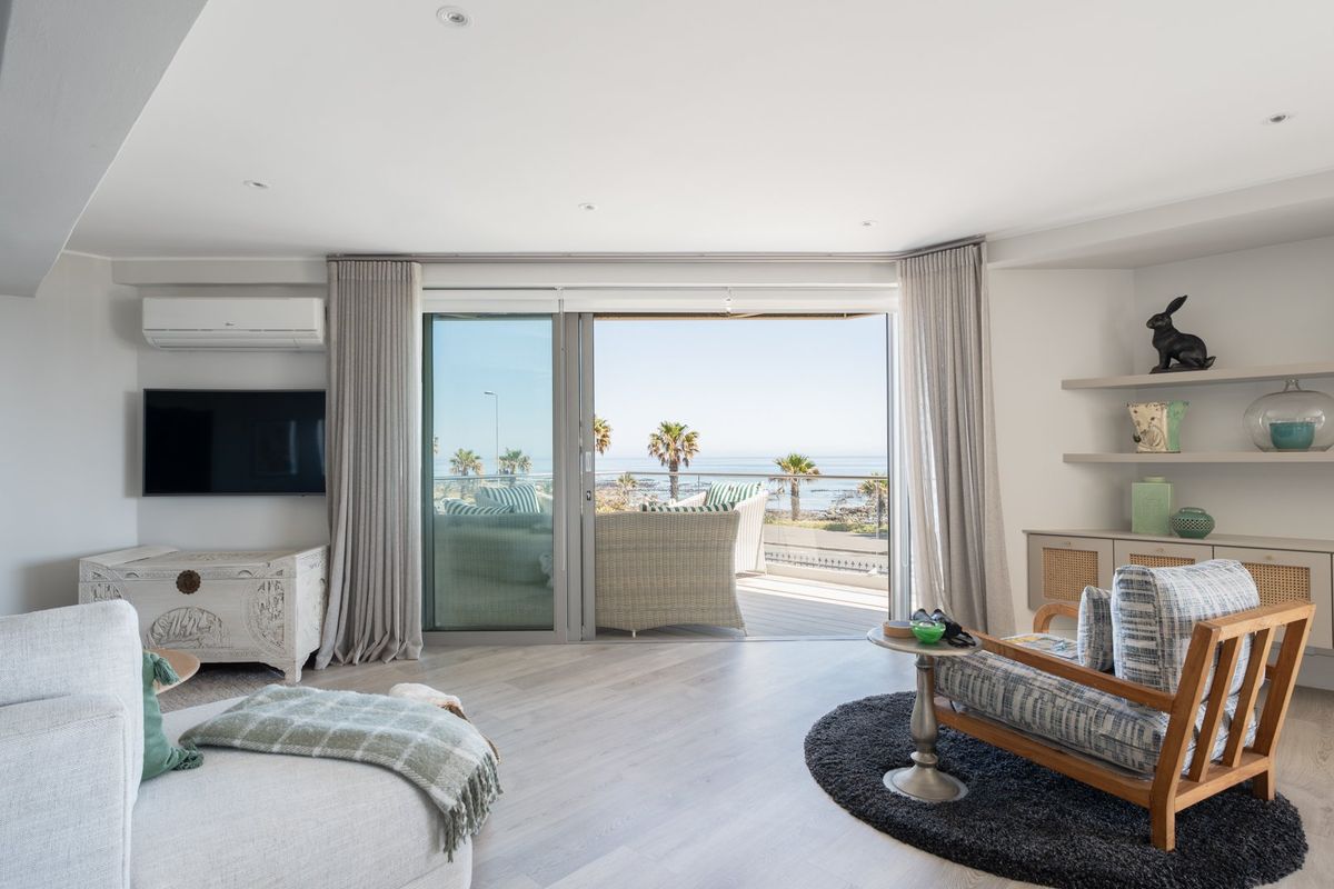 Bright living room featuring light wood-look flooring, built-in shelving, and large sliding glass doors opening to a balcony with ocean views.