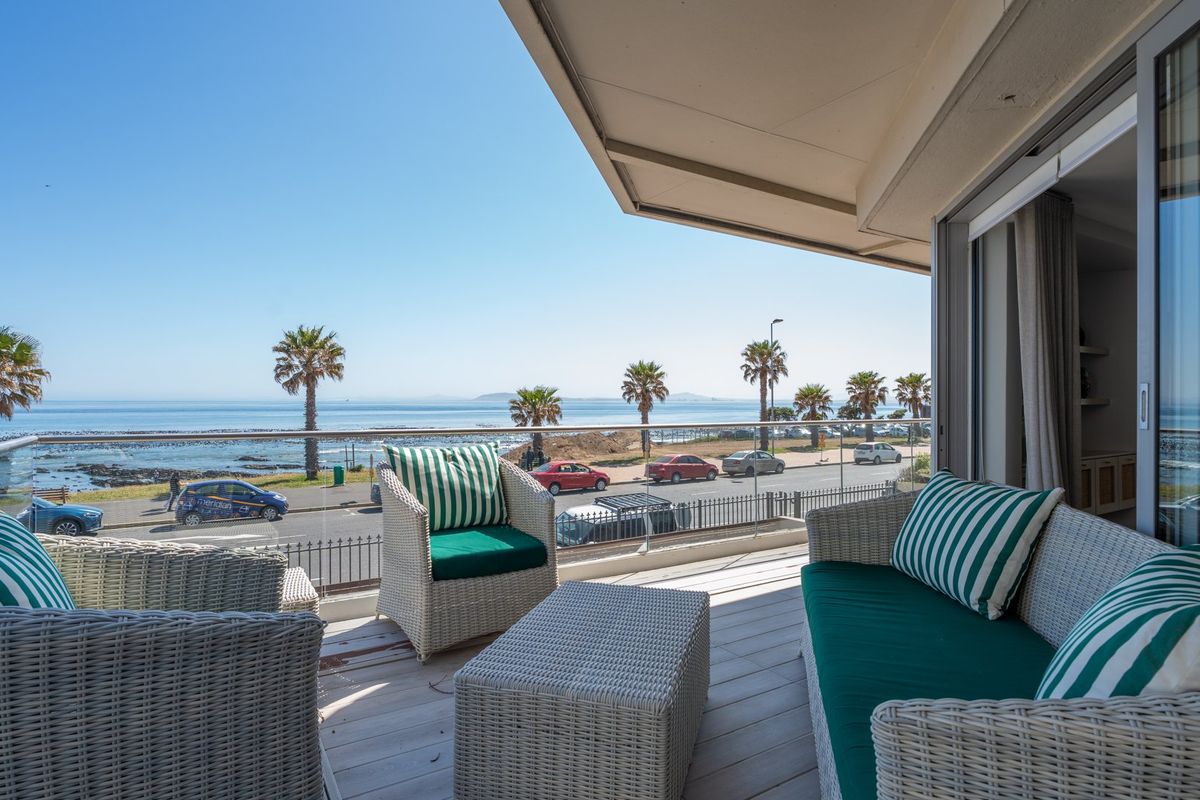 A spacious balcony featuring a glass balustrade and wooden decking, offering expansive ocean and coastal views.