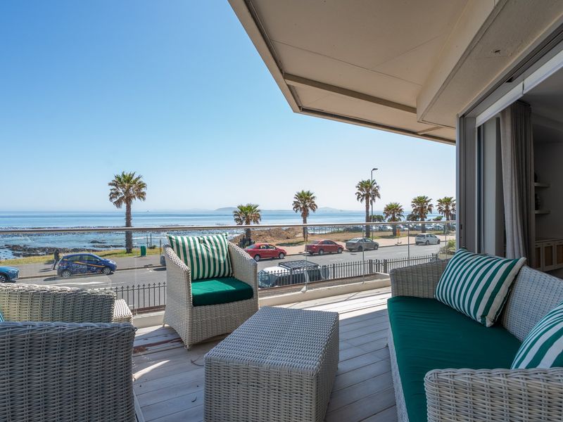 A spacious balcony featuring a glass balustrade and wooden decking, offering expansive ocean and coastal views.