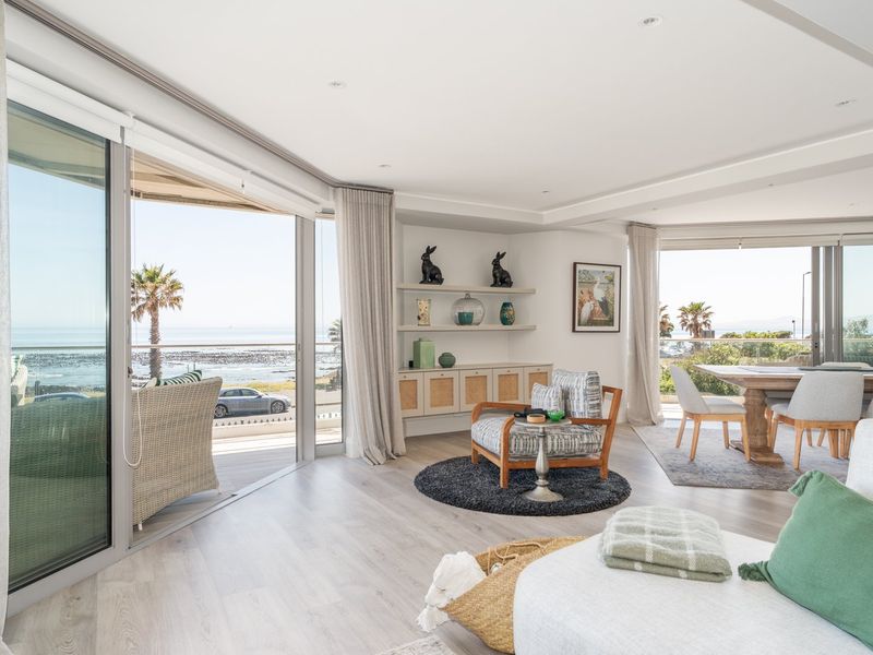 Bright open-plan living and dining area featuring floor-to-ceiling sliding glass doors that open onto a spacious balcony with scenic coastal views.