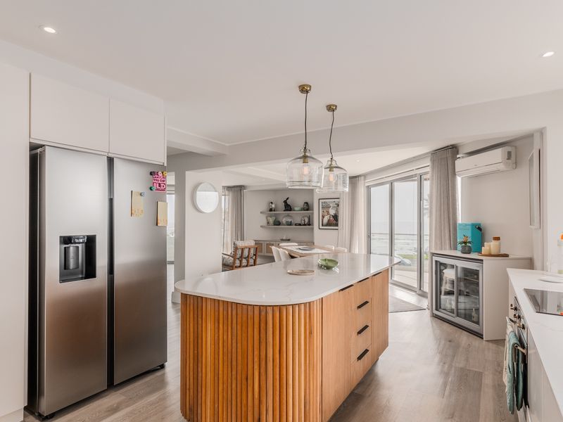 Modern open-plan kitchen featuring a central island with timber detailing, stone countertops, integrated cabinetry, and seamless flow to the living area and balcony.