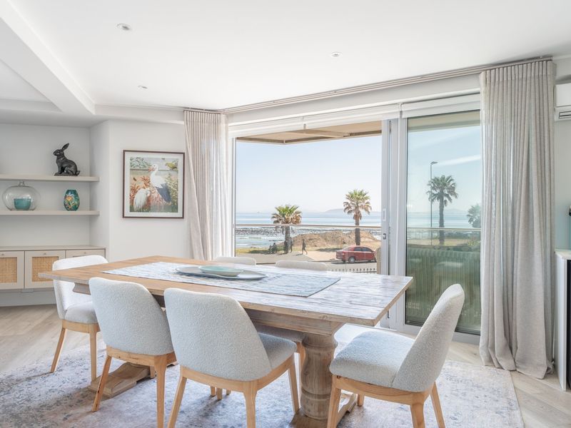 Bright open-plan dining area featuring built-in cabinetry, recessed lighting, and large sliding glass doors opening to a balcony with scenic coastal views.