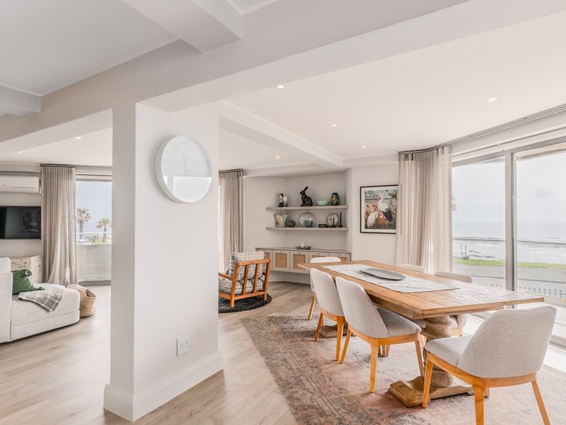Bright open-plan living and dining area featuring light wood-look flooring, recessed lighting, and large sliding glass doors offering expansive coastal views.