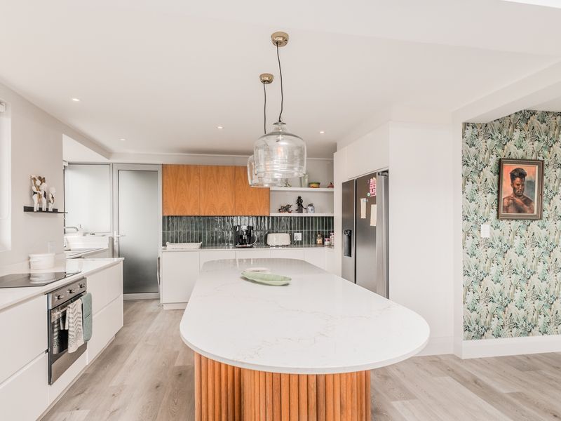 Modern open-plan kitchen featuring a large central island with stone countertop, sleek cabinetry, integrated appliances, and stylish tiled backsplash.