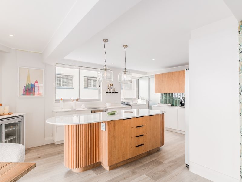Modern open-plan kitchen featuring a central island with wood-slat detailing, stone countertops, integrated cabinetry, and contemporary pendant lighting.
