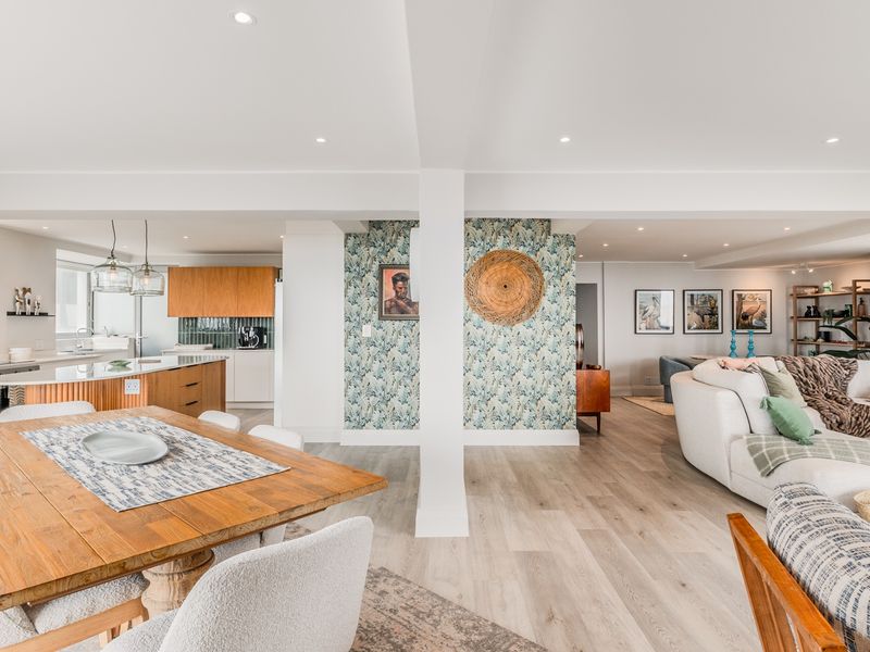 Spacious open-plan living area featuring a modern kitchen with a central island, dining space, and lounge, finished with light wood-look flooring and recessed lighting.