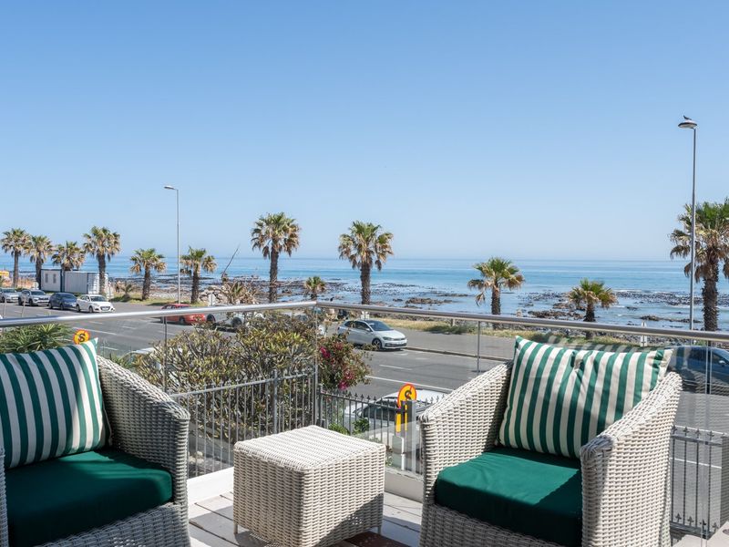 A spacious balcony offering panoramic coastal views, featuring a modern glass and metal balustrade overlooking the ocean and street front.