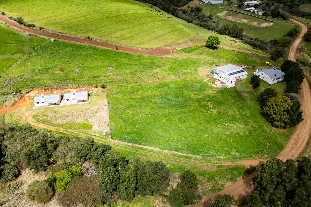 Aerial view of the farm property featuring multiple outbuildings, expansive green pasture, and established surrounding vegetation with gravel access roads.