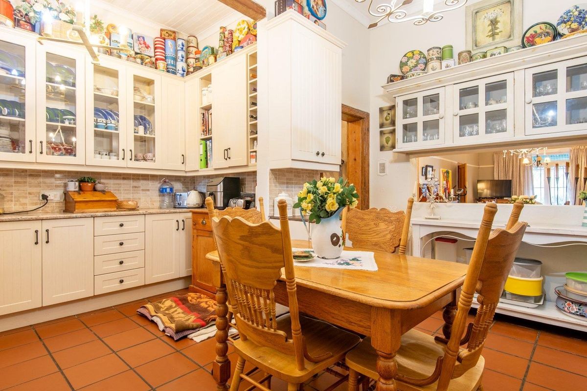 A traditional kitchen featuring extensive white cabinetry, tiled backsplash, and terracotta floor tiles, offering a warm and functional cooking and dining space.