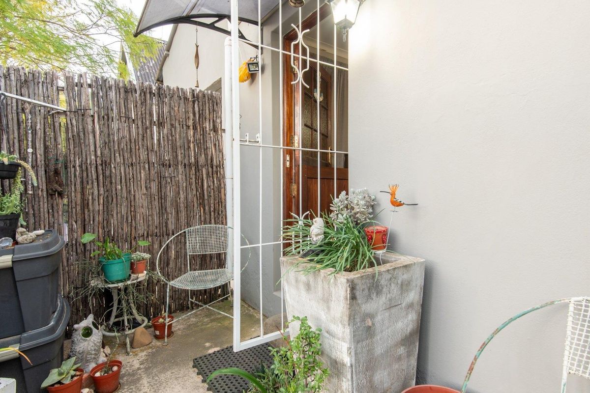 A small, private outdoor entrance area featuring a security gate, concrete flooring, and a rustic reed privacy screen.