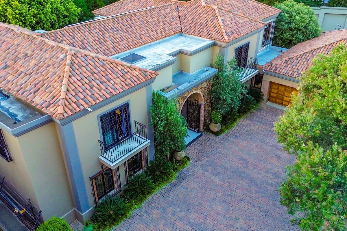 Aerial view of a multi-story residence featuring a terracotta tiled roof, paved driveway, and wrought iron balcony railings.