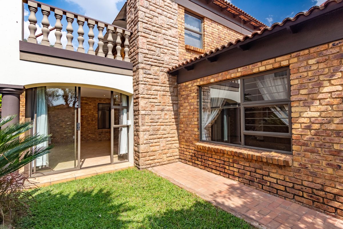 A view of the rear exterior featuring a brick facade, a paved walkway, a small lawn, and an upper-level balcony with stone balustrades.